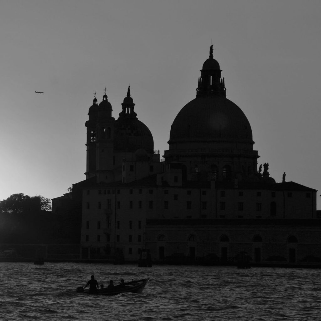 Photo en noir et blanc de Santa Maria della Salute à Venise, avec une barque et un avion.