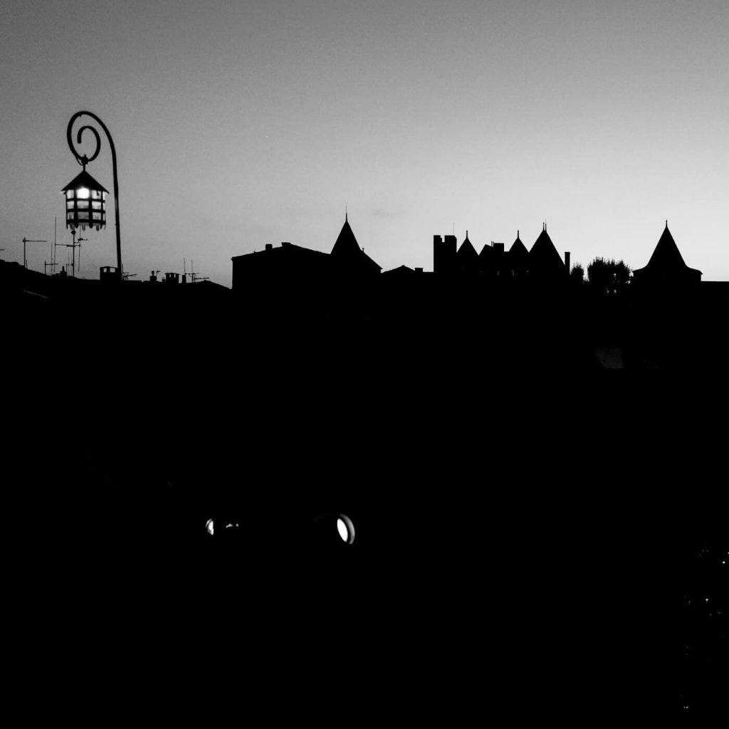 Photo en noir et blanc des remparts de Carcassonne la nuit, avec une lanterne.