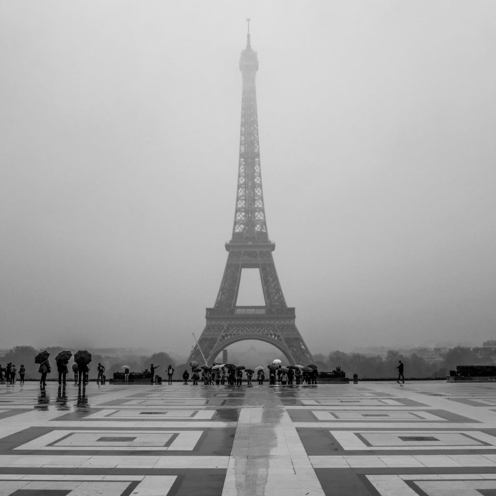Photo en noir et blanc de la Tour Eiffel à Paris un jour de pluie, avec des touristes sous leurs parapluies.