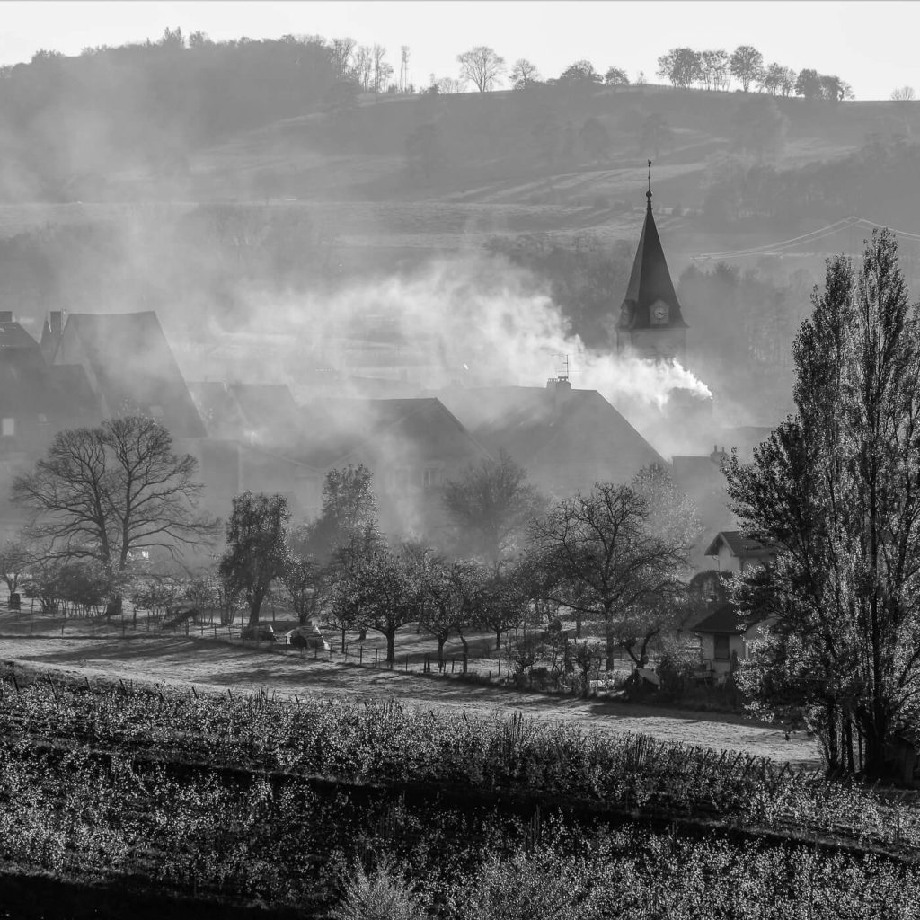 Photo en noir et blanc du village de Lavigny sous la fumée, dans le Jura en France.